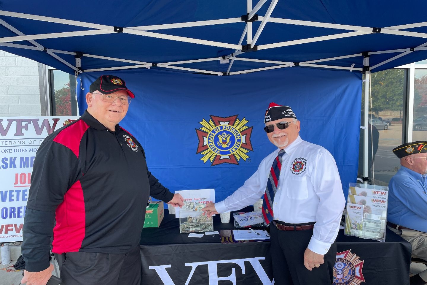 Howard Lowdermilk and Joe Csuka are shown entering a $100 bill received from a Wake Forest citizen into the donation container. The VFW partners with Sport Clips each year leading into Veterans' Day to raise money for the Help-a-Hero Scholarship Fund. This provides scholarships for higher education to Active Military and Veterans.